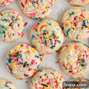 Funfetti Butter Cookies Recipe with Sprinkle-Filled Shortbread 13 Funfetti butter cookies topped with sparkling sugar placed randomly on a white sheet of parchment paper.