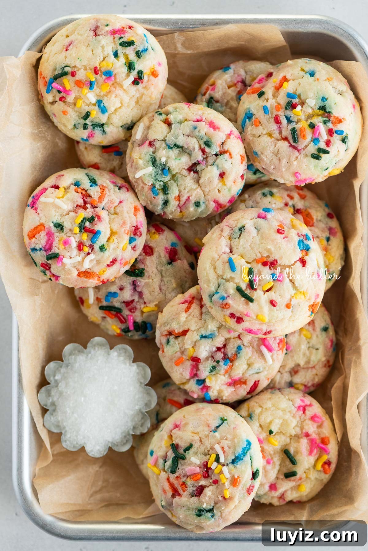 Funfetti Butter Cookies Recipe with Sprinkle-Filled Shortbread 3 Parchment paper lined small baking sheet filled with funfetti butter cookies and a small scalloped bowl of white sparkling sugar.