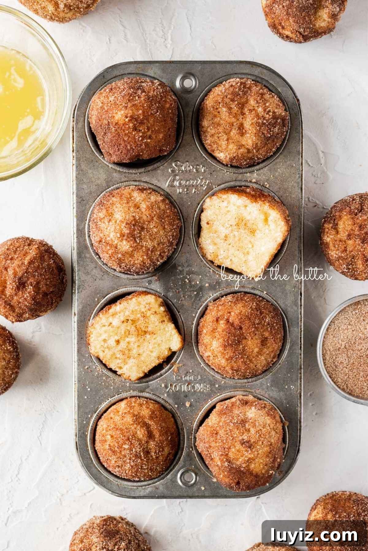 Mini French Breakfast Puffs: Airy, Jam-Filled Pastry Bites 4 Mini french breakfast puffs placed in vintage metal muffin tin with bowls of cinnamon sugar and melted butter placed around them on a white textured background.