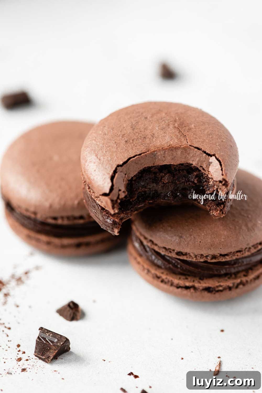 Decadent Dark Chocolate Macarons Recipe for Perfect Crisps 13 Angled image of stacked chocolate macarons with the top one having a bite taken out of it | All Images © Beyond the Butter™