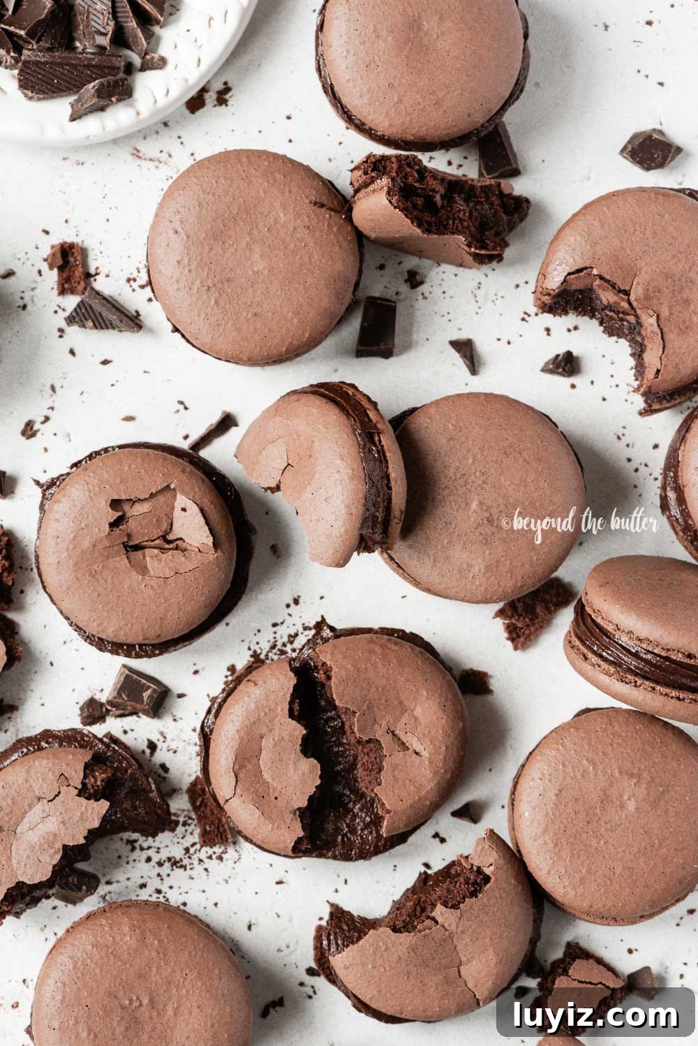 Decadent Dark Chocolate Macarons Recipe for Perfect Crisps 9 Scattered dark chocolate macarons with some broken or pulled apart | All Images © Beyond the Butter™