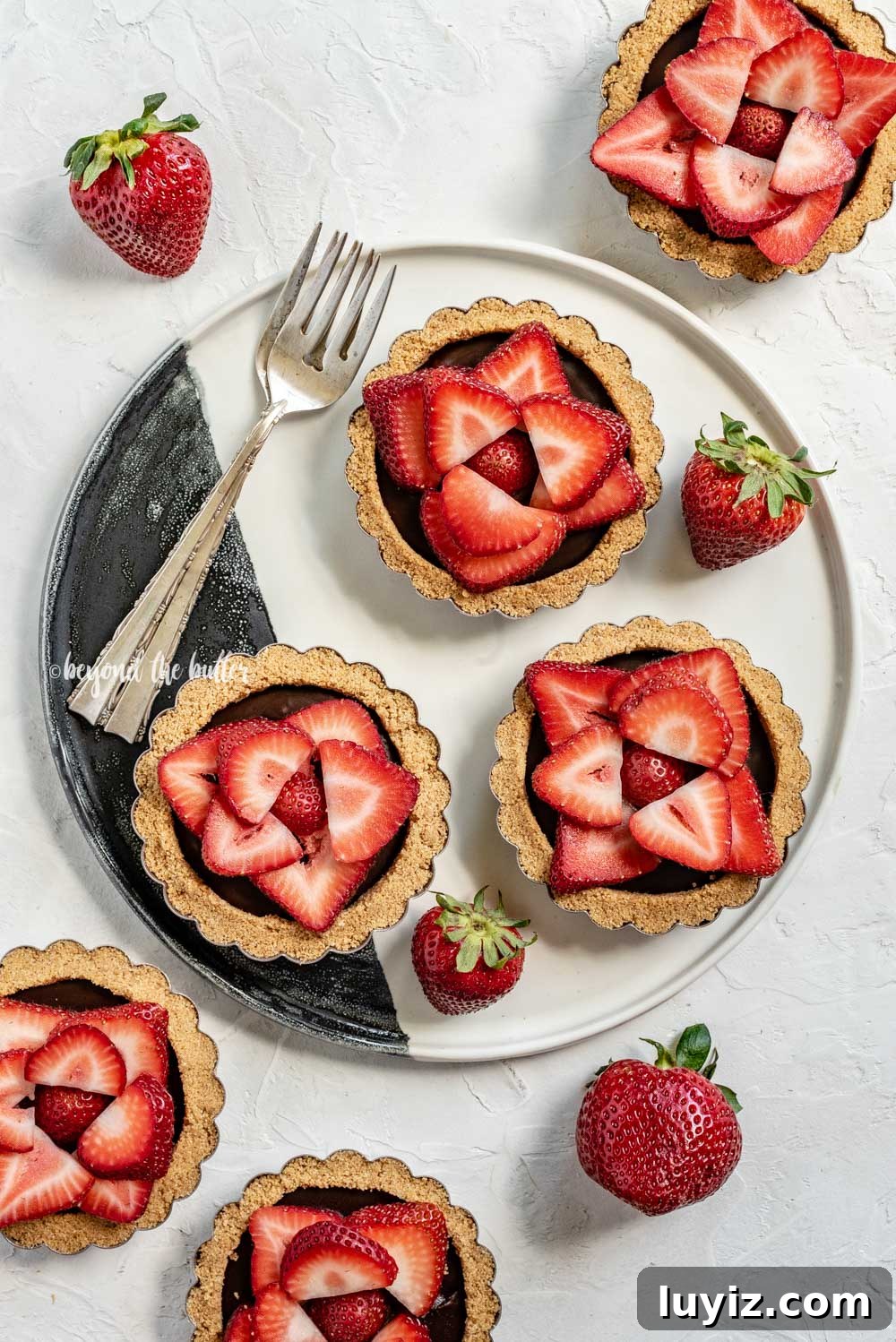 Mini Strawberry Nutella Tartlets: Bite-Sized Dessert Recipe 6 Overhead image of 6 mini strawberry nutella tarts on a black and white serving plate and randomly placed strawberries | All Images © Beyond the Butter™