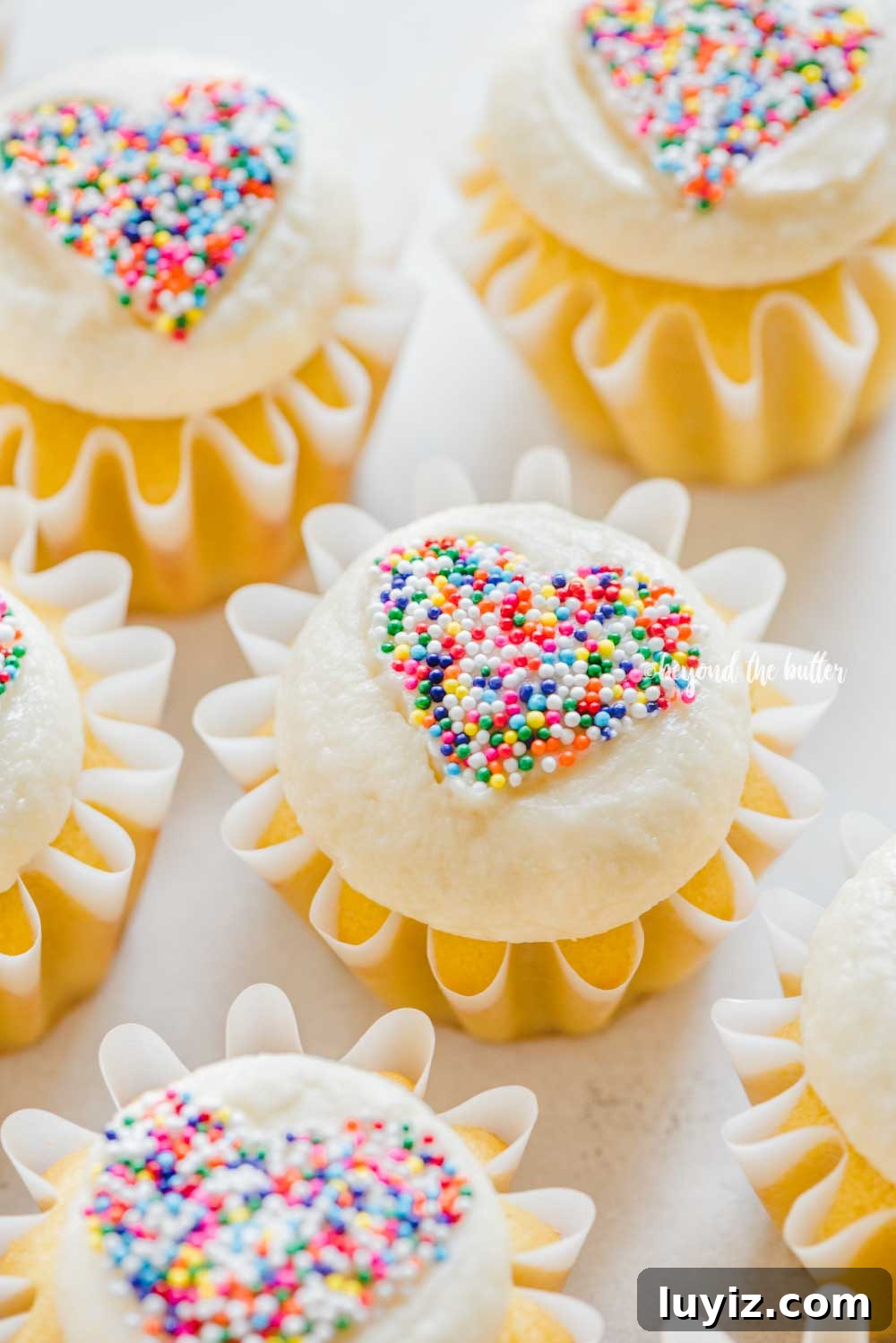 How to Make Sprinkled Heart Cupcakes: Step-by-Step Tutorial 3 Angled image of sprinkled heart cupcakes on white/gray background | All Images © Beyond the Butter™