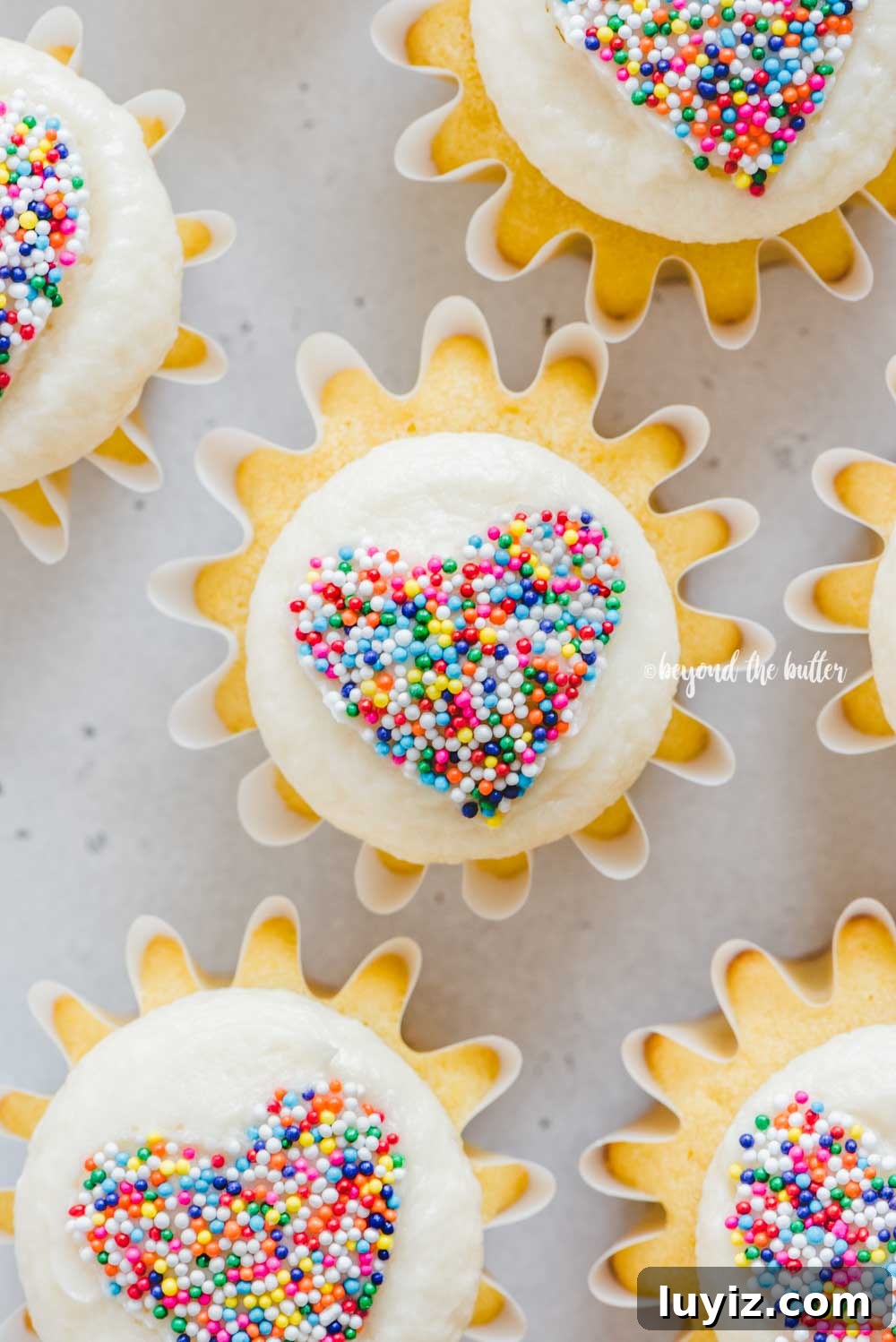 How to Make Sprinkled Heart Cupcakes: Step-by-Step Tutorial 9 Overhead image of sprinkled heart cupcakes on white/gray background | All Images © Beyond the Butter™