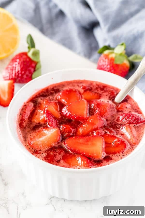 A white dish of strawberry sauce with strawberries in the background.