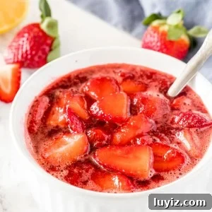 A white dish of strawberry sauce with strawberries in the background.