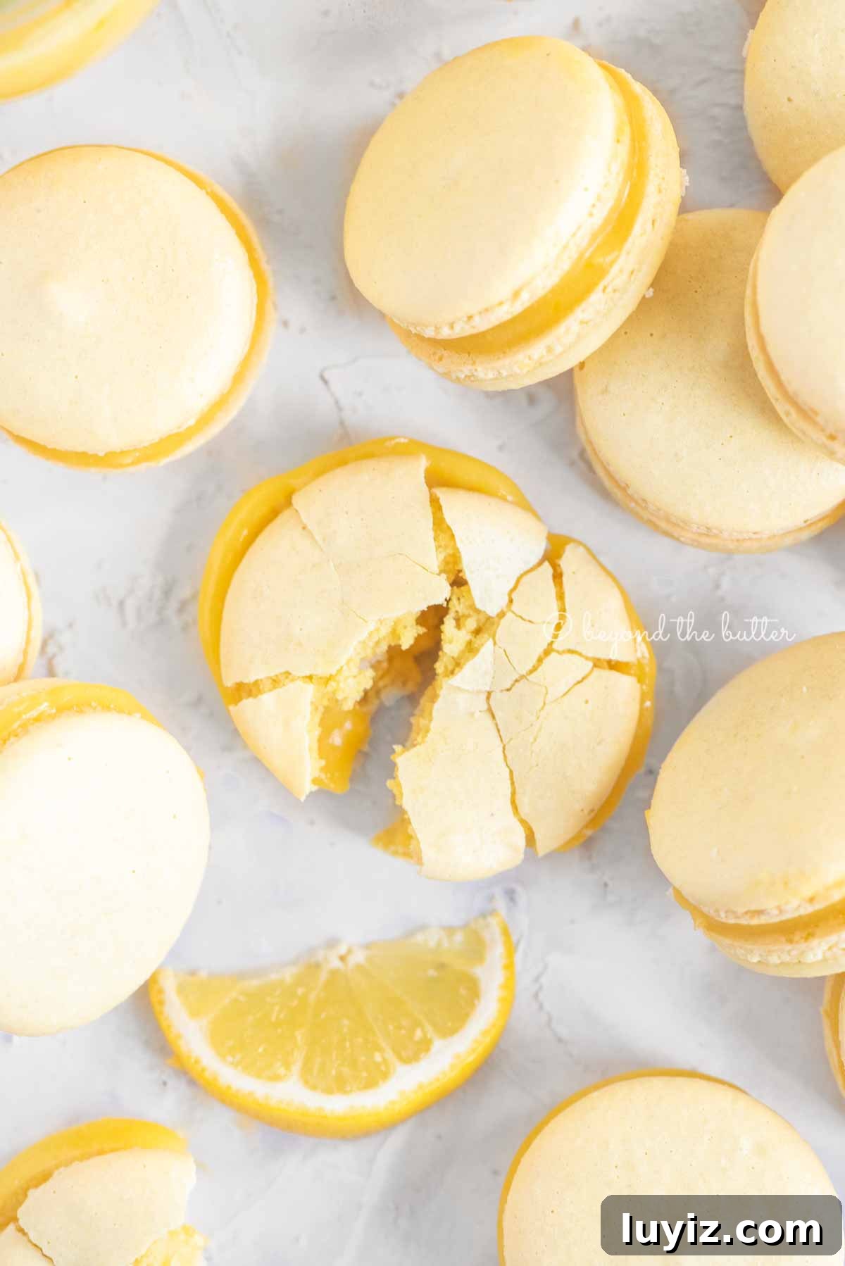 Zesty Lemon Bar Macarons: Tangy Citrus Sandwich Cookies 7 Overhead image randomly placed lemon macarons with the center macaron broken apart | All Images © Beyond the Butter™