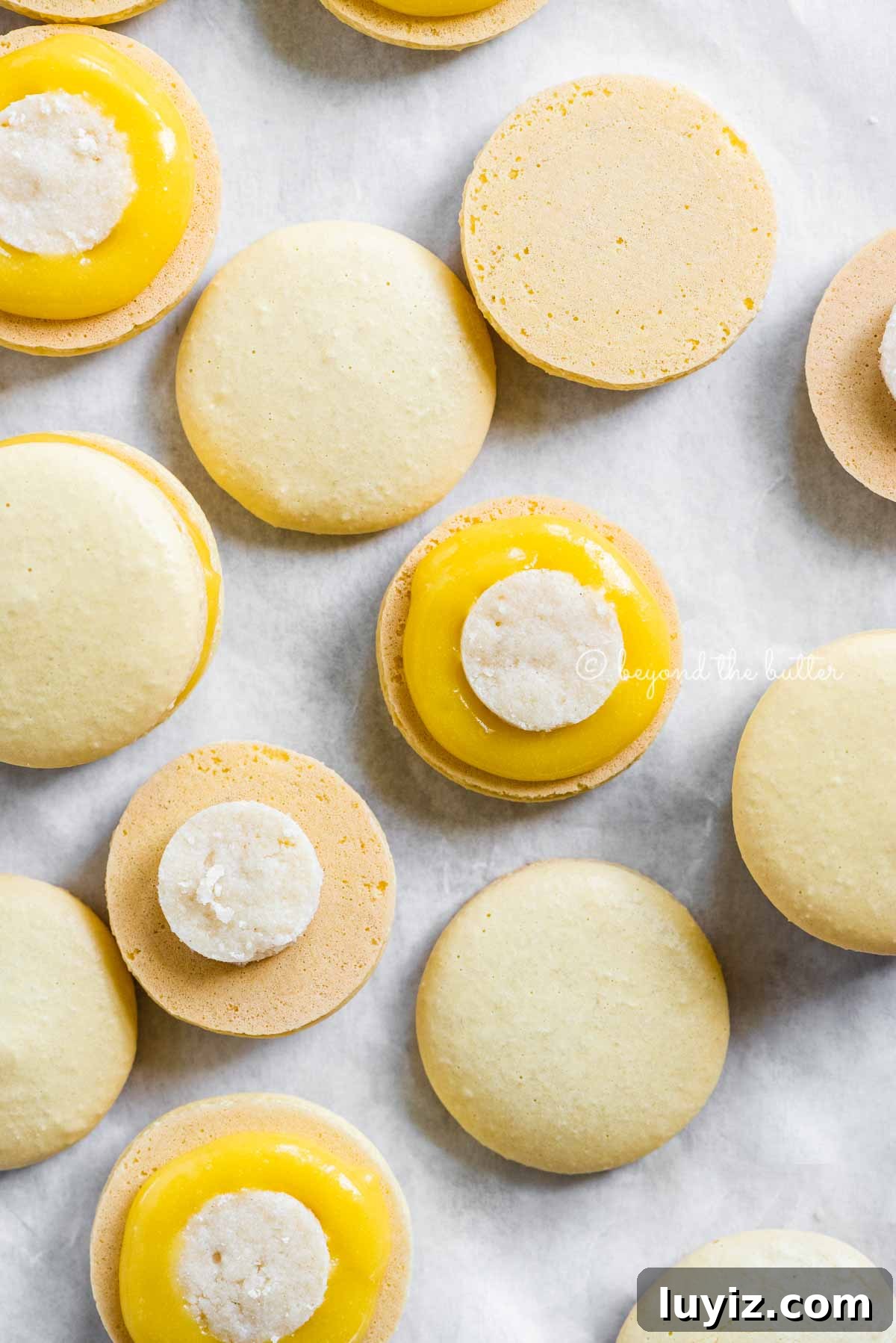 Zesty Lemon Bar Macarons: Tangy Citrus Sandwich Cookies 10 Overhead image of lemon bar macarons half opened topped with shortbread crust centers and lemon curd filling | All Images © Beyond the Butter™