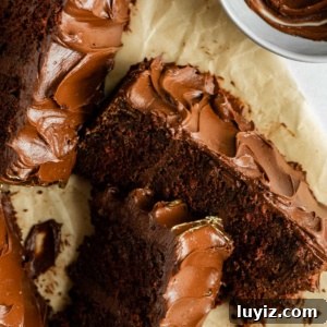 Moist Chocolate Zucchini Cake Recipe with Cocoa and Oil 11 Overhead image of chocolate zucchini cake slices on parchment paper with a small bowl of frosting.