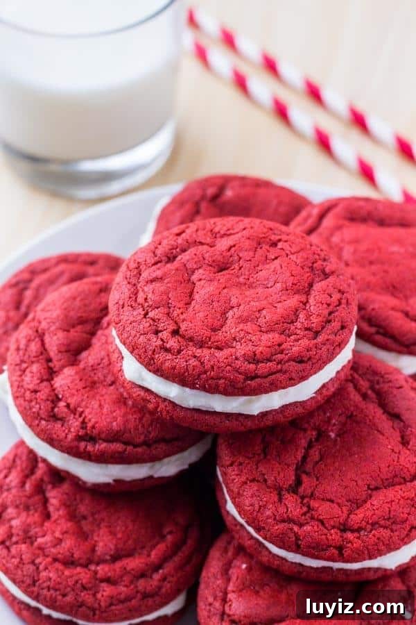 Red Velvet Sandwich Cookie Recipe — Soft Cream-Filled Cookies 3 A plate of red velvet sandwich cookies with cream cheese frosting and a glass of milk.