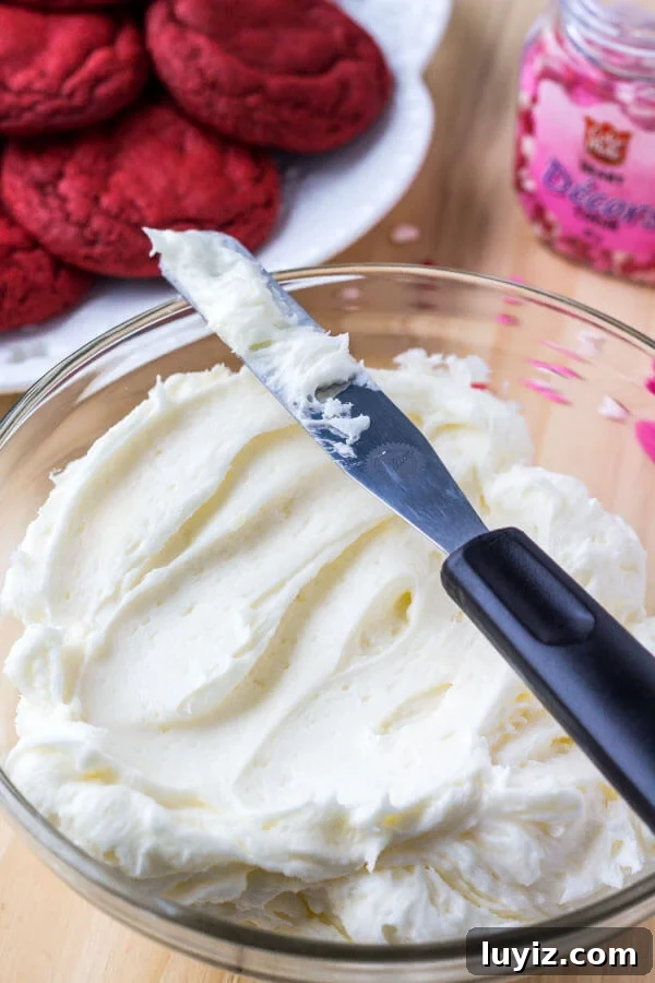 Red Velvet Sandwich Cookie Recipe — Soft Cream-Filled Cookies 4 A bowl of fluffy cream cheese buttercream ready for frosting on red velvet cookies.