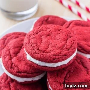 Red Velvet Sandwich Cookie Recipe — Soft Cream-Filled Cookies 6 A plate of red velvet sandwich cookies with cream cheese frosting and a glass of milk.