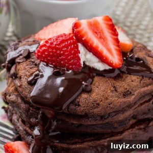 A stack of fluffy chocolate pancakes with chocolate ganache, strawberries and whipped cream is the ultimate breakfast for chocolate lovers.