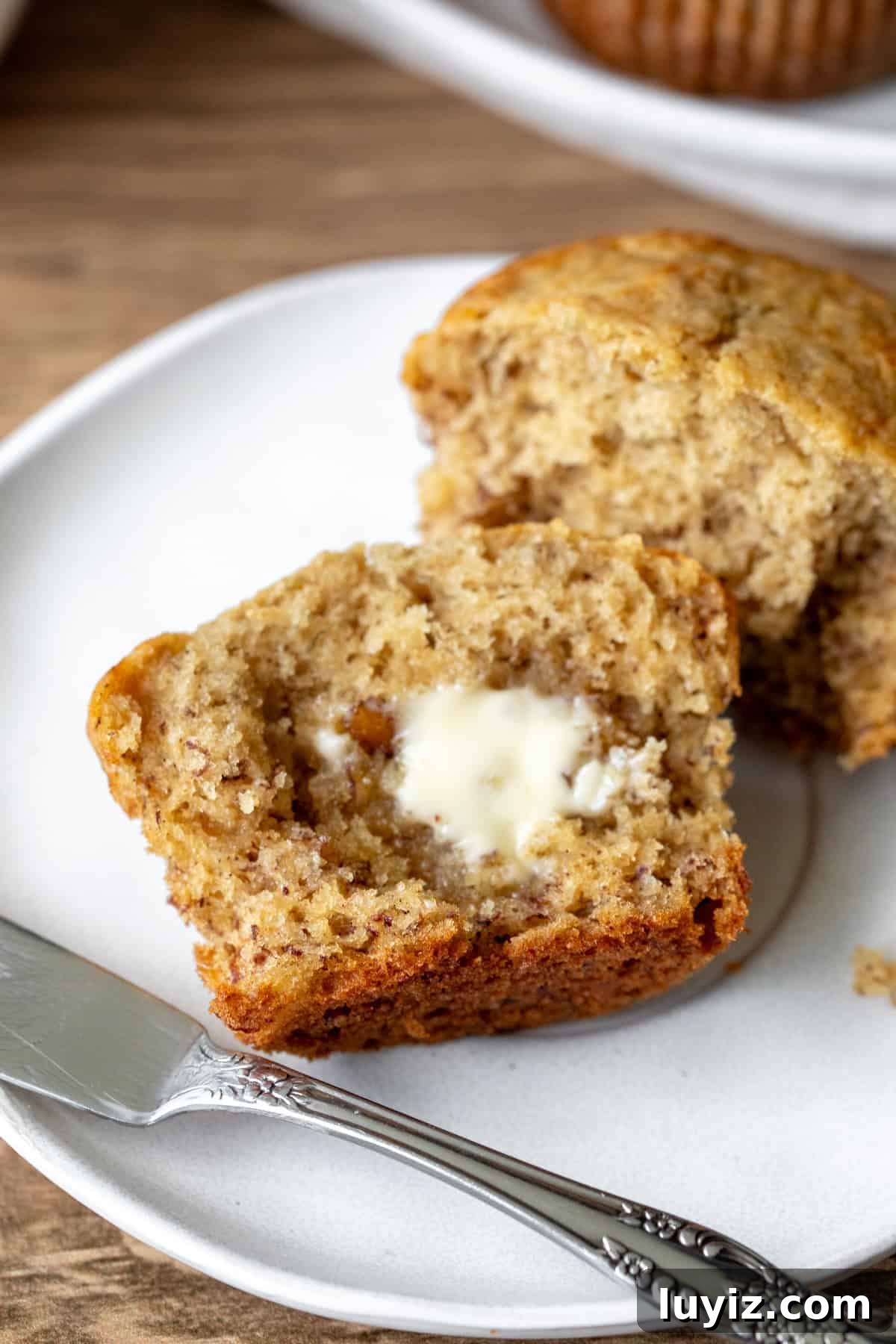 Moist Banana Bread Muffins with Cinnamon Streusel 7 Banana muffin broken in half on a plate, with butter spread on the muffin