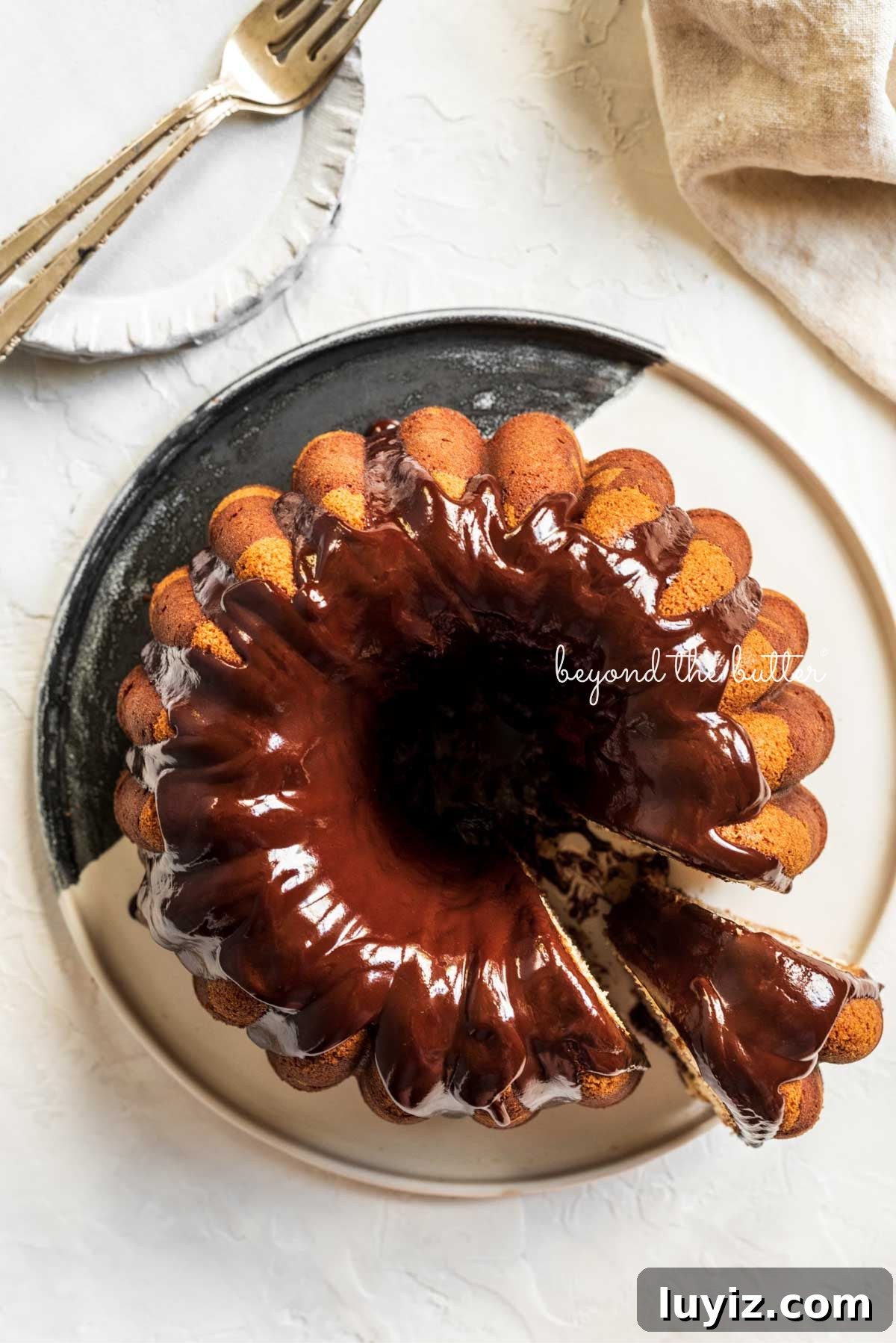 Decadent Marble Bundt Cake Recipe with Swirled Chocolate-Vanilla 15 Marble bundt cake on a black and white ceramic dessert plate with chocolate ganache glaze drizzled over the top with a a slice partially removed.