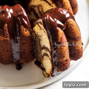 Decadent Marble Bundt Cake Recipe with Swirled Chocolate-Vanilla 20 Chocolate glazed marble bundt cake with one slice partially removed on a white ceramic dessert plate and white background.