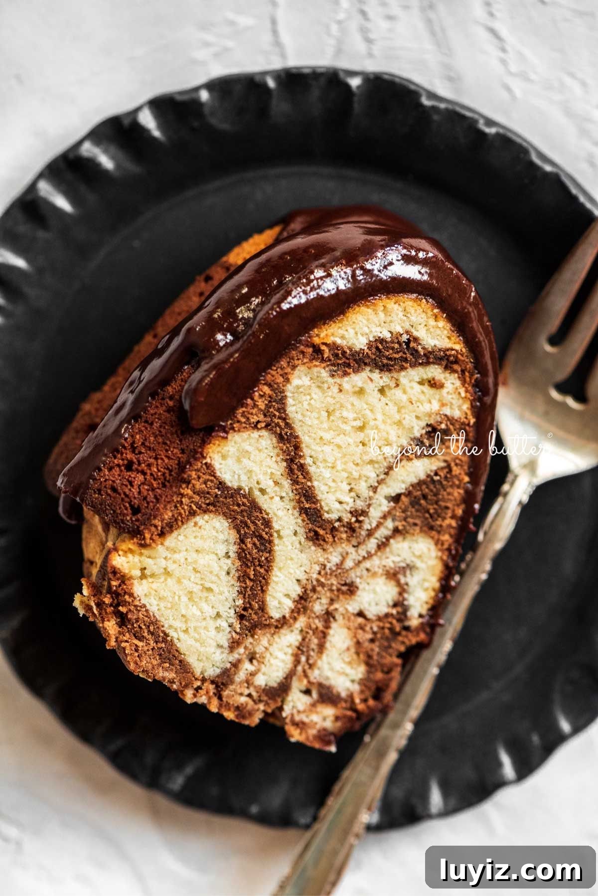 Decadent Marble Bundt Cake Recipe with Swirled Chocolate-Vanilla 3 Slice of marble bundt cake on black dessert plate with fork placed next to it on a white background.