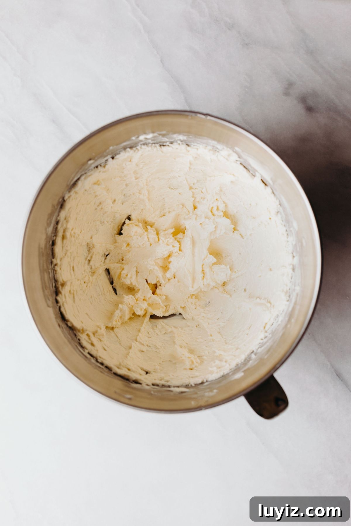 Decadent Marble Bundt Cake Recipe with Swirled Chocolate-Vanilla 5 Beaten cream cheese and unsalted butter in a stainless steel mixing bowl on a white marbled background.