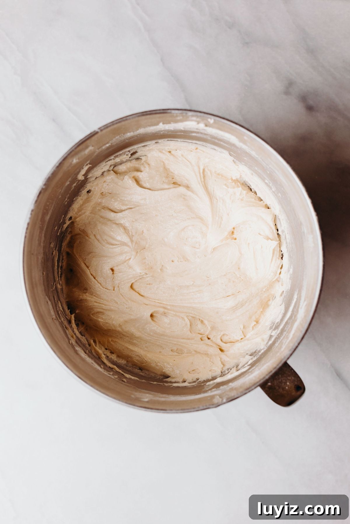 Decadent Marble Bundt Cake Recipe with Swirled Chocolate-Vanilla 7 Bundt cake batter after adding the eggs and flour in a stainless steel mixing bowl on a white marbled background.