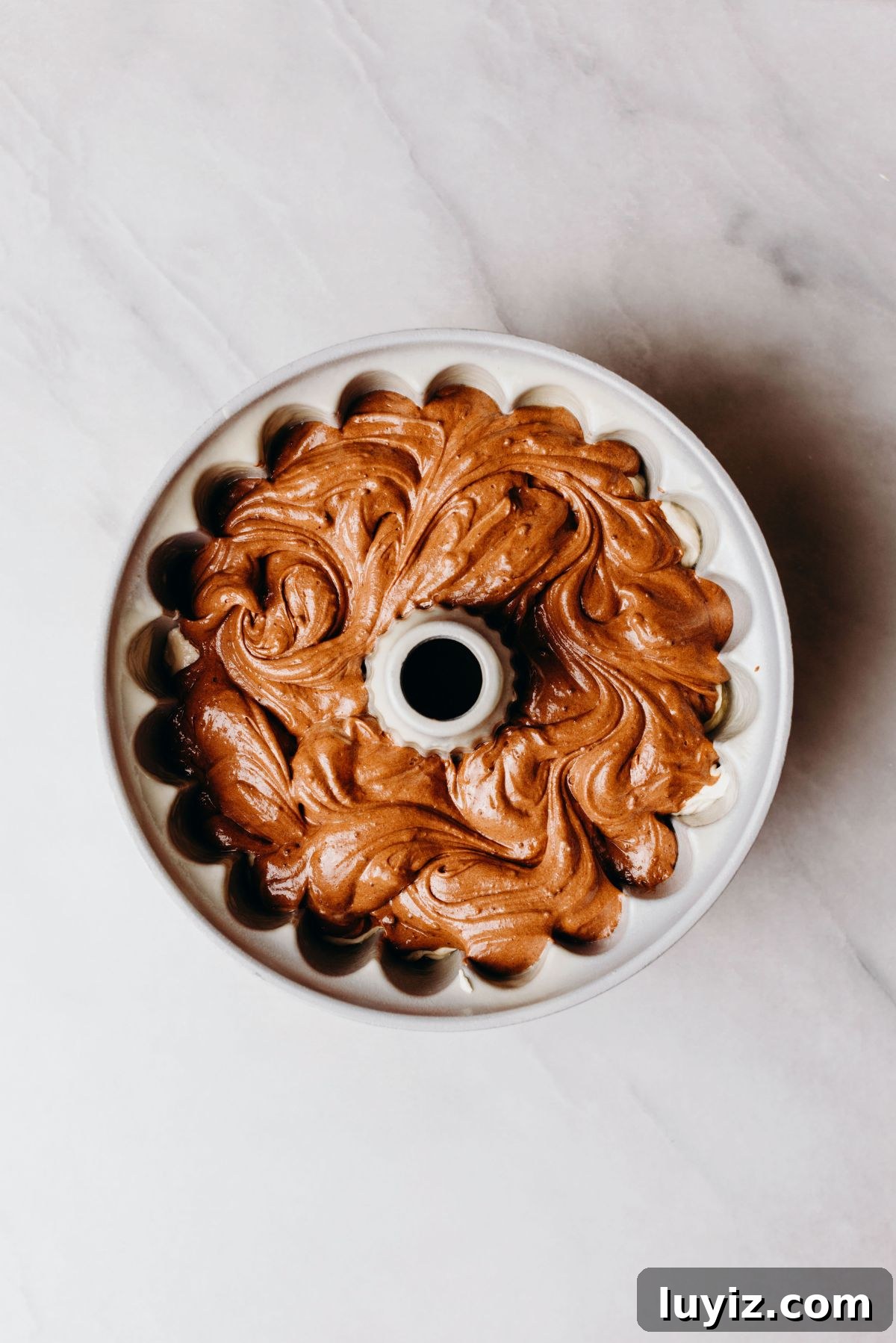 Decadent Marble Bundt Cake Recipe with Swirled Chocolate-Vanilla 10 Swirled chocolate and vanilla cake batter in a bundt cake pan on a white marbled background.