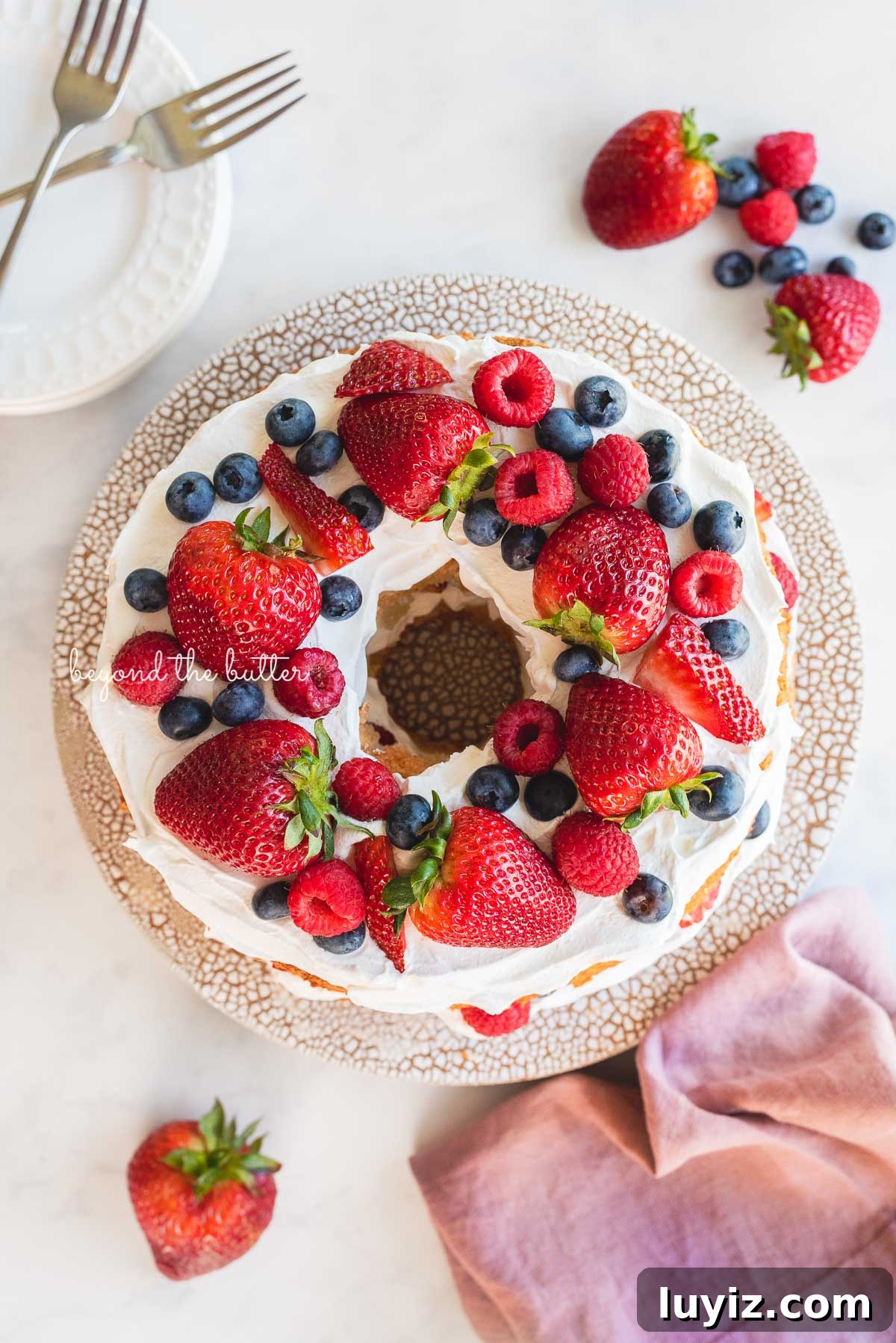 Light and Fluffy Homemade Angel Food Cake Recipe 5 Homemade angel food cake on ceramic cake stand surrounded by dessert plates and fresh berries