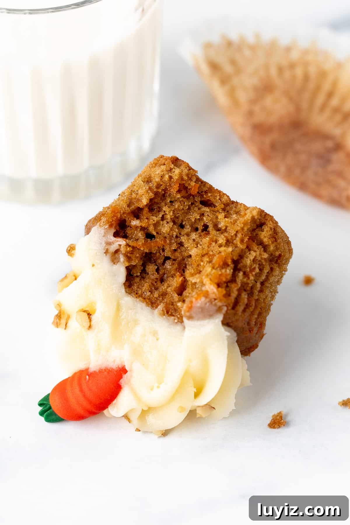 Moist Carrot Cupcakes with Cream Cheese Frosting 6 Carrot cake cupcake with a bite taken out, on its side with glass of milk
