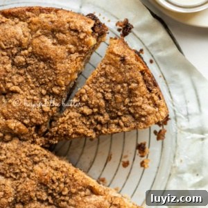 Apple Cinnamon Coffee Cake Recipe for Moist, Tender Crumbs 13 Apple coffee cake on a parchment paper lined wire cooling rack with slices removed and a simple vanilla glaze to the side.