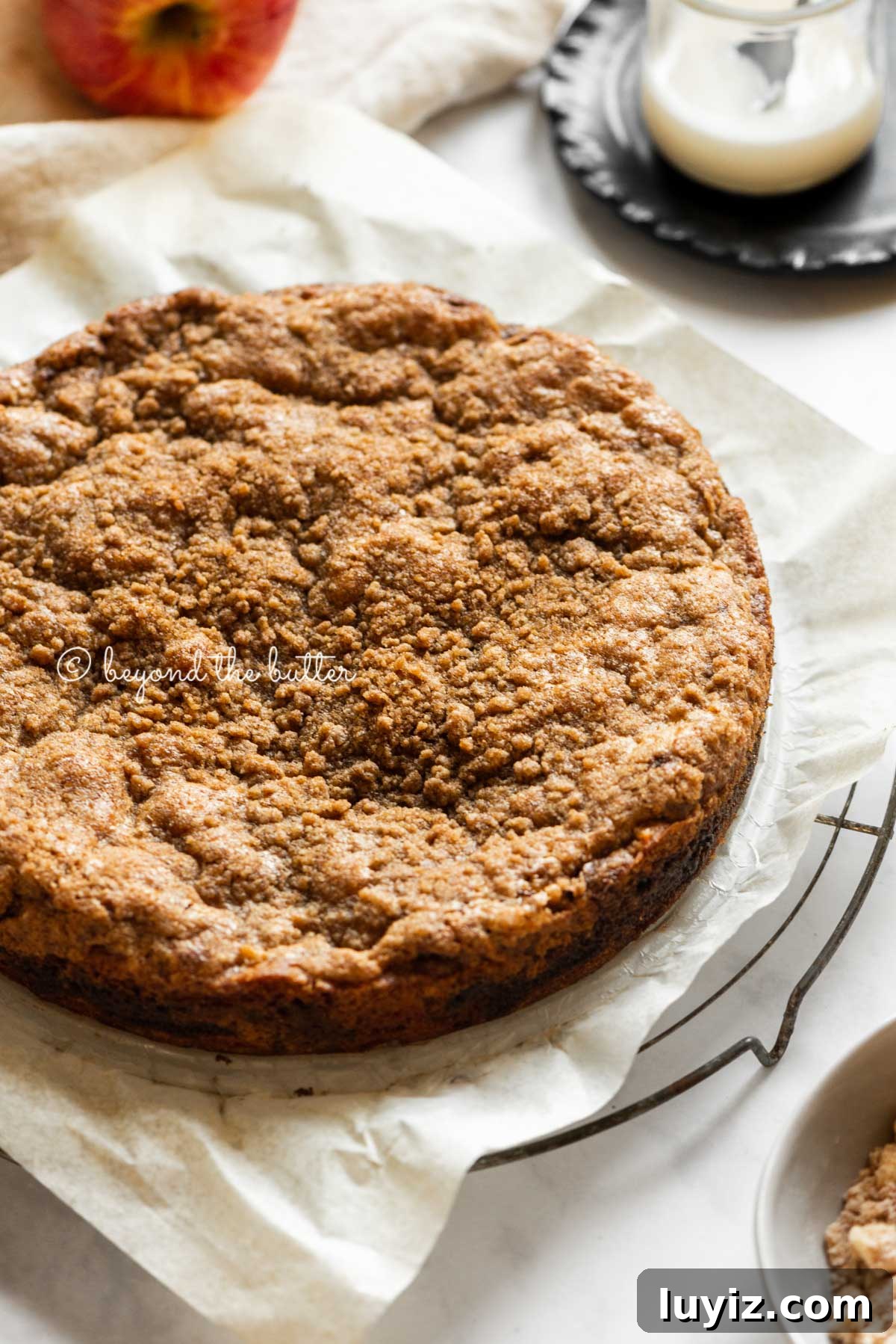 Apple Cinnamon Coffee Cake Recipe for Moist, Tender Crumbs 3 Cinnamon apple coffee cake cooling on a parchment paper lined cooling rack with a glass of a simple vanilla glaze off to the side | All Images © Beyond the Butter™
