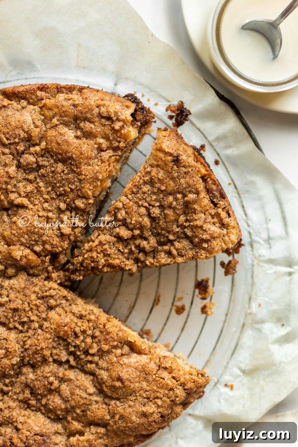Apple Cinnamon Coffee Cake Recipe for Moist, Tender Crumbs 4 Apple coffee cake on a parchment paper lined wire cooling rack with slices removed and a simple vanilla glaze to the side | All Images © Beyond the Butter™