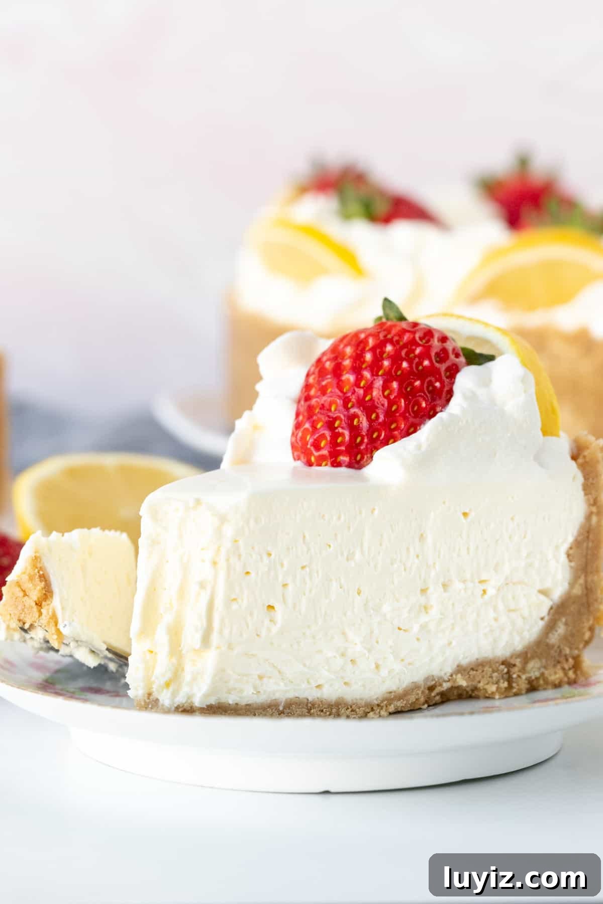 Creamy No-Bake Lemon Cheesecake Recipe: Zesty Dessert Without Baking 9 Piece of no-bake lemon cheesecake topped with whipped cream and a strawberry, with a bite taken out