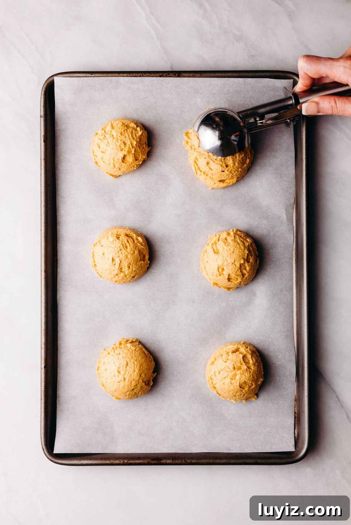 Pumpkin Whoopie Pies Recipe: Soft Spiced Sandwich Cookies 11 Scooping pumpkin whoopie pie batter onto a parchment paper lined baking sheet on a light grey marbled background.