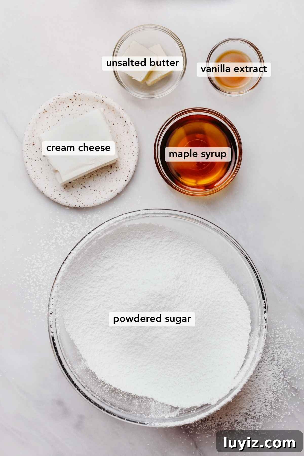 Pumpkin Whoopie Pies Recipe: Soft Spiced Sandwich Cookies 6 Ingredients in various size bowls labeled as unsalted butter, vanilla extract, cream cheese, maple syrup, and powdered sugar on a white marbled background.