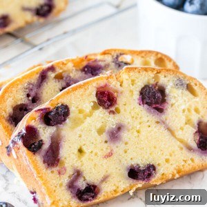 3 slices of moist blueberry bread with the rest of the loaf on a cooling rack in the background.