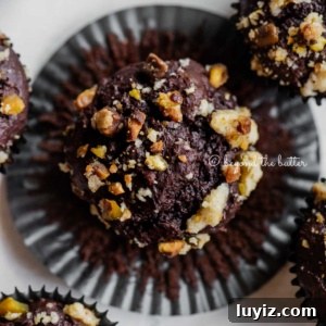 Dark Chocolate Pistachio Cream Cheese Muffins Recipe 12 Dark chocolate pistachio cream cheese muffins with center muffin unwrapped on light gray background.