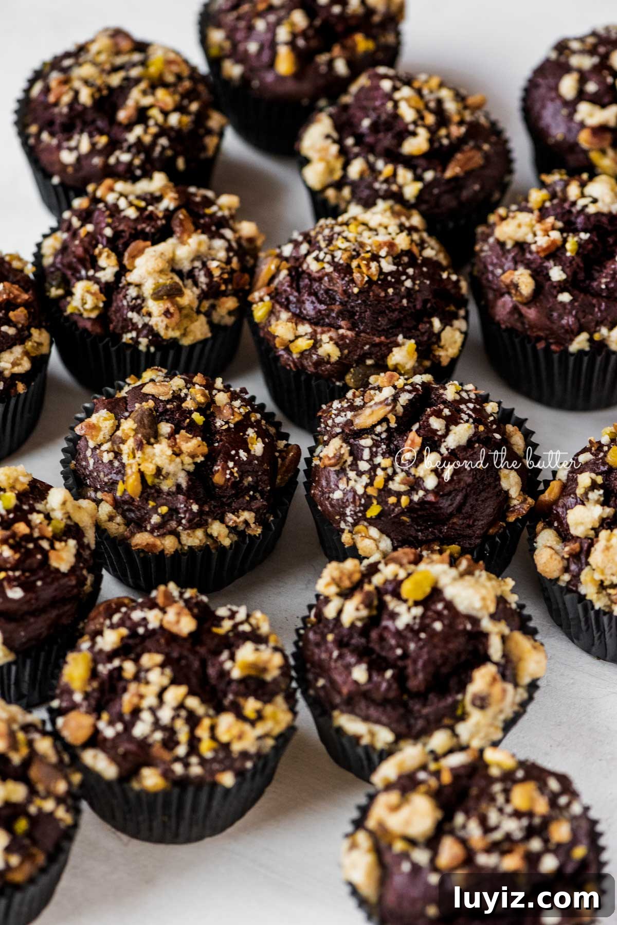 Dark Chocolate Pistachio Cream Cheese Muffins Recipe 3 Randomly placed dark chocolate pistachio cream cheese muffins on gray background | All Images © Beyond the Butter®