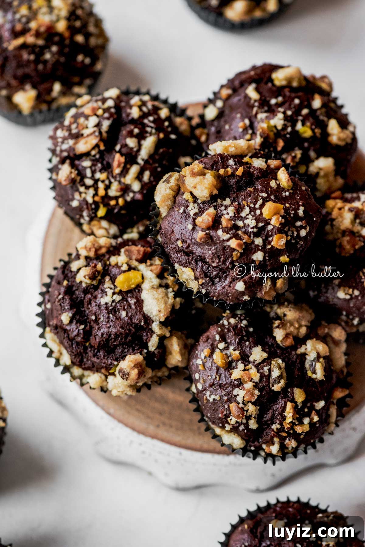 Dark Chocolate Pistachio Cream Cheese Muffins Recipe 6 Small plate of dark chocolate pistachio cream cheese muffins on gray background | All Images © Beyond the Butter®