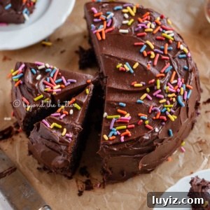 Decadent Single-Layer Chocolate Cake Recipe for One Pan 13 Angled image of sliced single layer chocolate cake on parchment paper with slices of cake on small dessert plates around it and a knife on parchment paper.