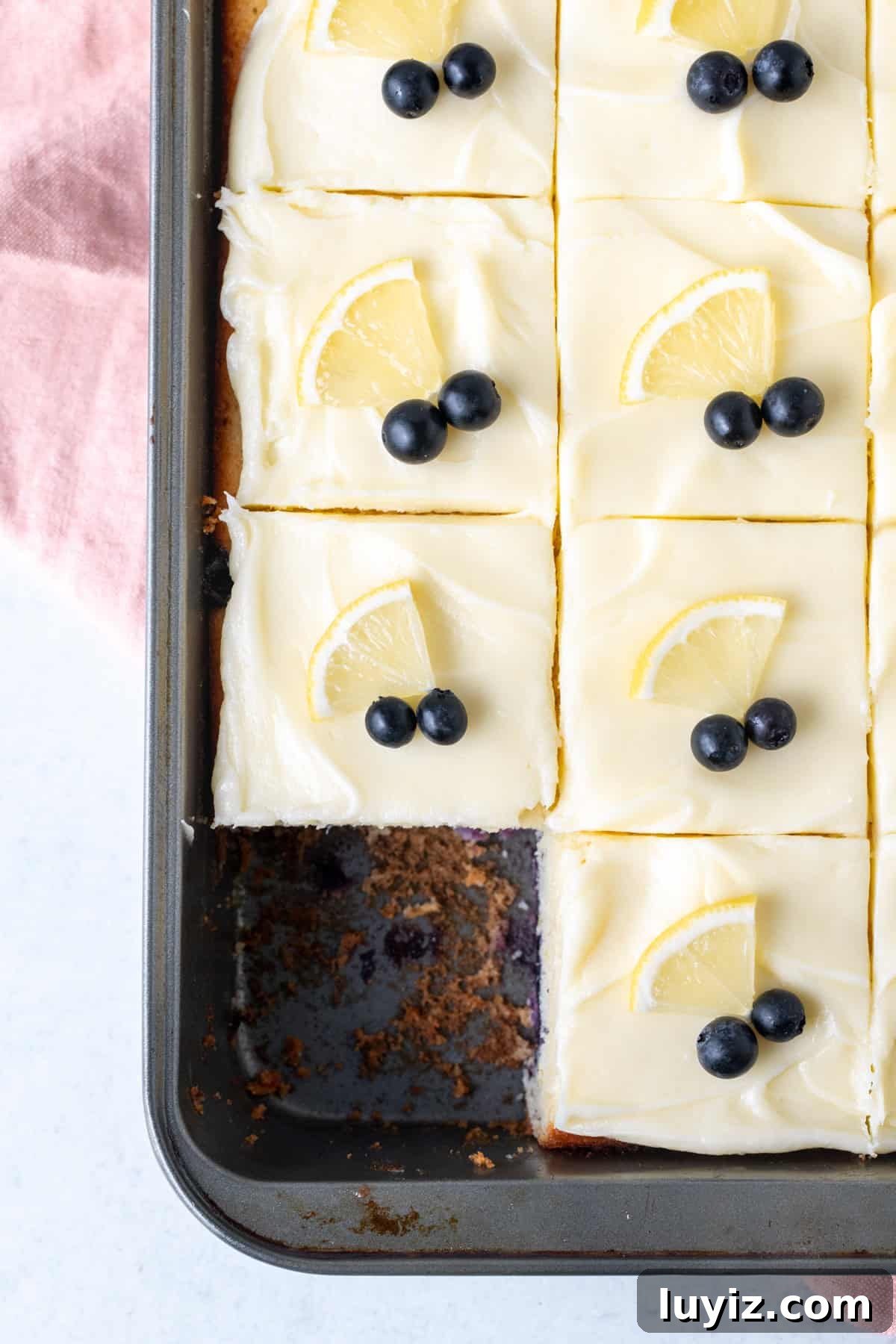 Lemon Blueberry Layer Cake Recipe with Zesty Glaze 3 9x13 inch sheet pan of lemon blueberry cake with cream cheese frosting, cut into squares.