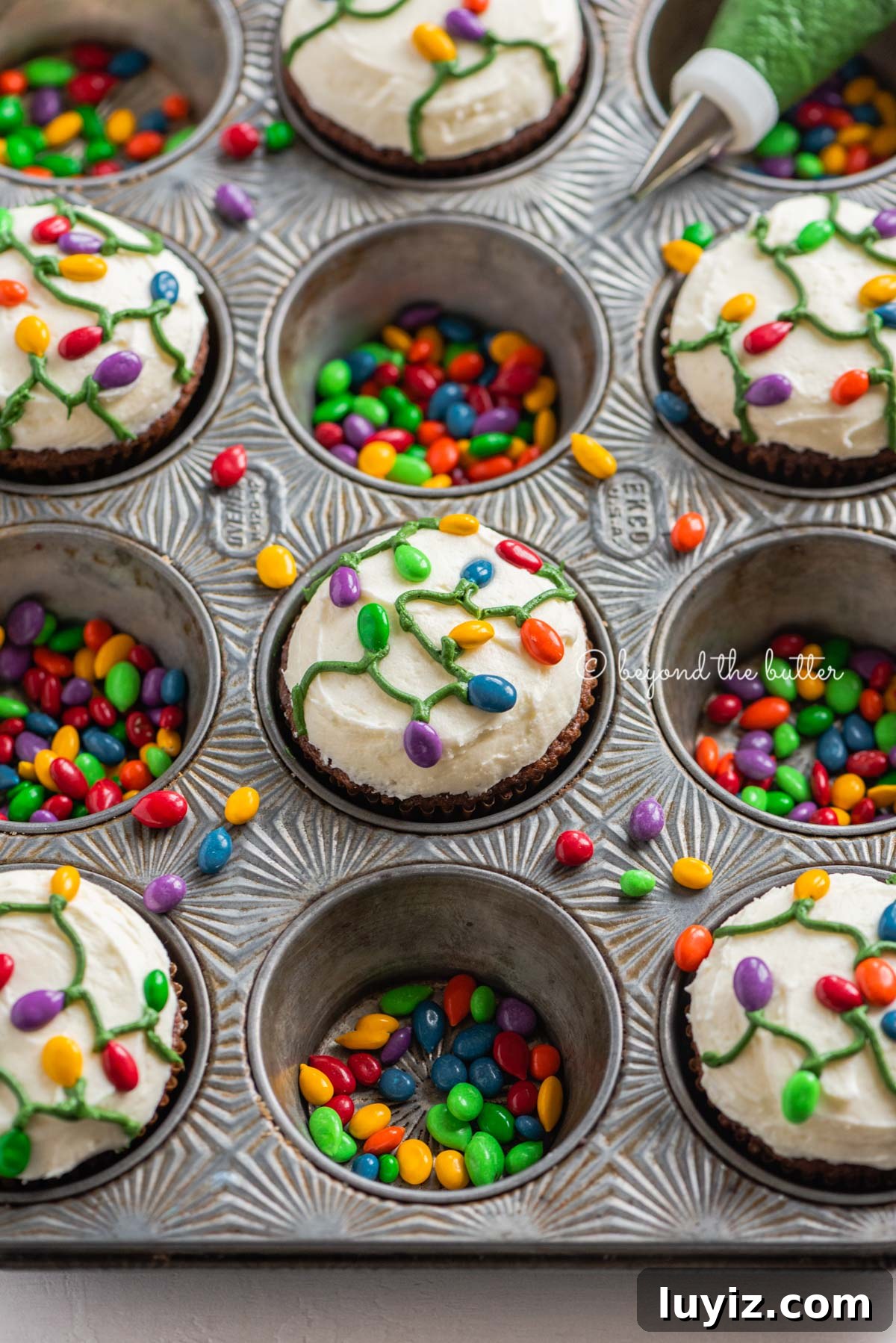 Gingerbread Cupcakes Recipe for a Small Batch (6 Muffins) 5 Cupcake tin with decorated small batch gingerbread cupcakes with marshmallow frosting and rainbow chocolate covered sunflower seeds | All Images © Beyond the Butter®