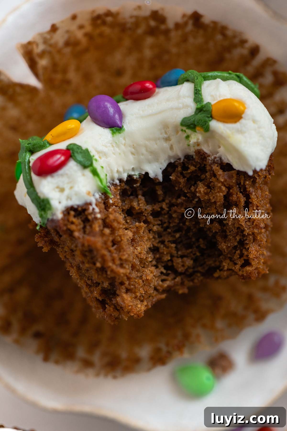 Gingerbread Cupcakes Recipe for a Small Batch (6 Muffins) 6 Liner removed with bite taken out of it gingerbread cupcake on a small dessert plate on a white, chocolate covered sunflower seed background | All Images © Beyond the Butter®