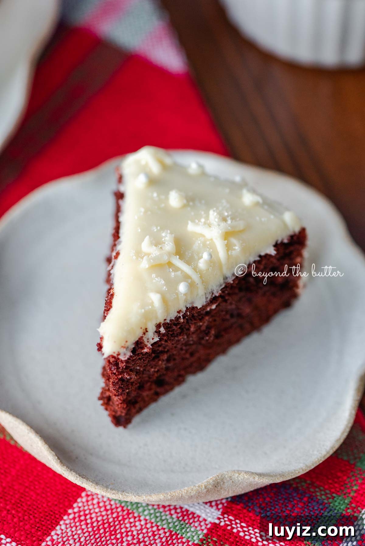 Simple Single-Layer Red Velvet Cake Recipe for Perfect Results 3 Slice of red velvet cake with cream cheese frosting on a scalloped edge dessert plate with red plaid background | All Images © Beyond the Butter®