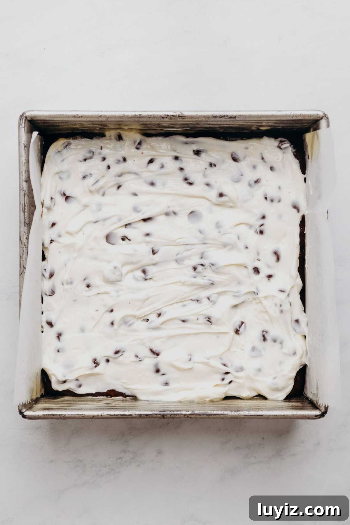 Cream Cheese Swirled Chocolate Chip Brownies 13 Brownie batter spread in a pan with cream cheese filling on top.