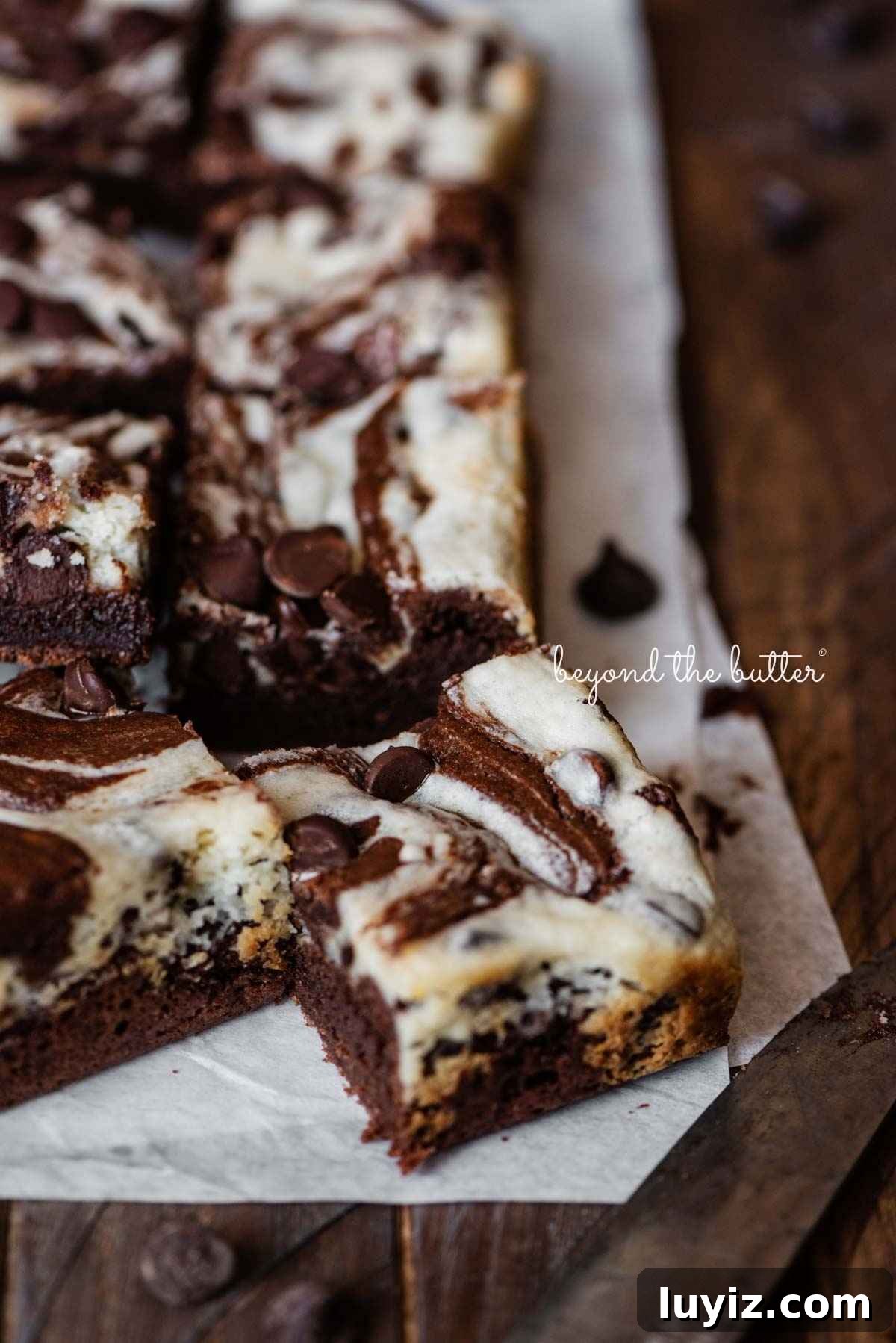 Cream Cheese Swirled Chocolate Chip Brownies 17 Chocolate chip cream cheese brownies on parchment paper on a dark wood table.