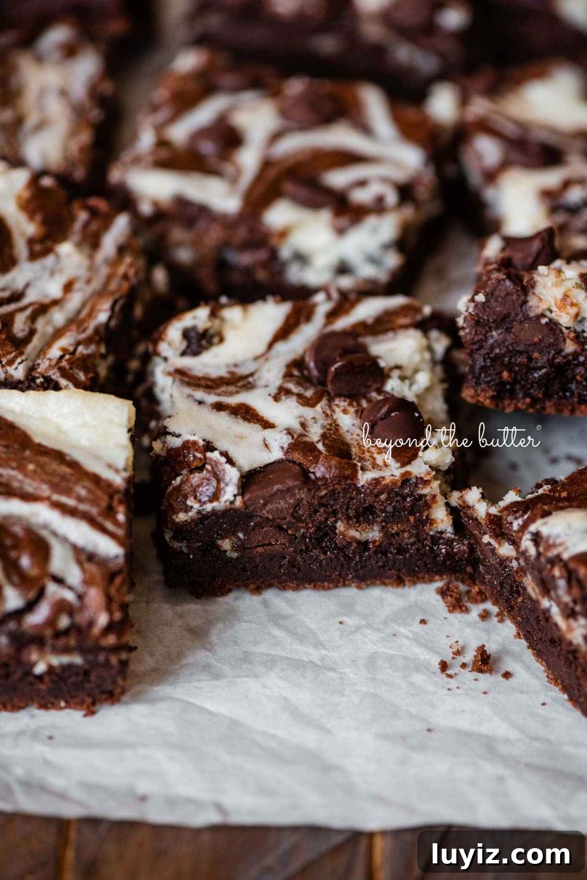 Cream Cheese Swirled Chocolate Chip Brownies 4 Sliced chocolate chip cream cheese brownies on white parchment paper on a dark wood background.