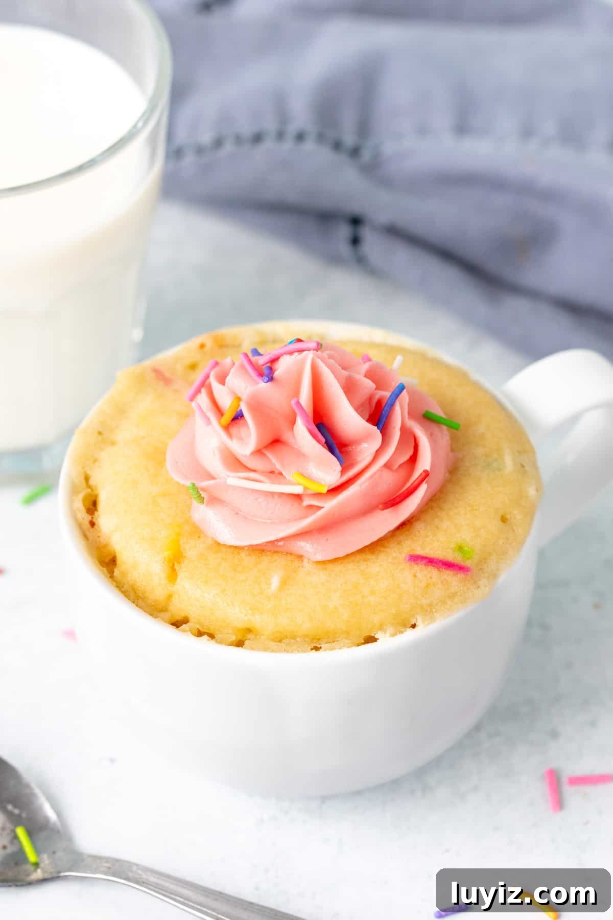 Quick Vanilla Mug Cake Recipe for One — Ready in Minutes 2 Vanilla mug cake topped with pink frosting and sprinkles with a glass of milk