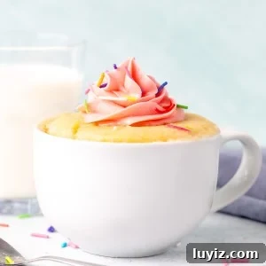 Vanilla mug cake decorated with pink frosting with a glass of milk