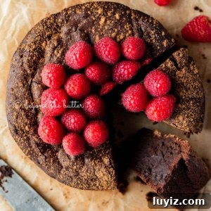 Flourless Mini Chocolate Cake Recipe for Rich Dessert 14 Sliced small flourless chocolate cake topped with cocoa powder and fresh raspberries on parchment paper.