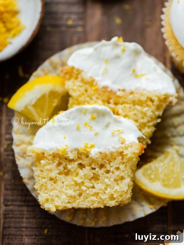Decadent Black Bottom Cupcakes with Cream Cheese Swirl 18 Sliced open lemon cupcake with whipped lemon cream cheese frosting on cupake liner and 2 wedges of lemons on a dark wood background.