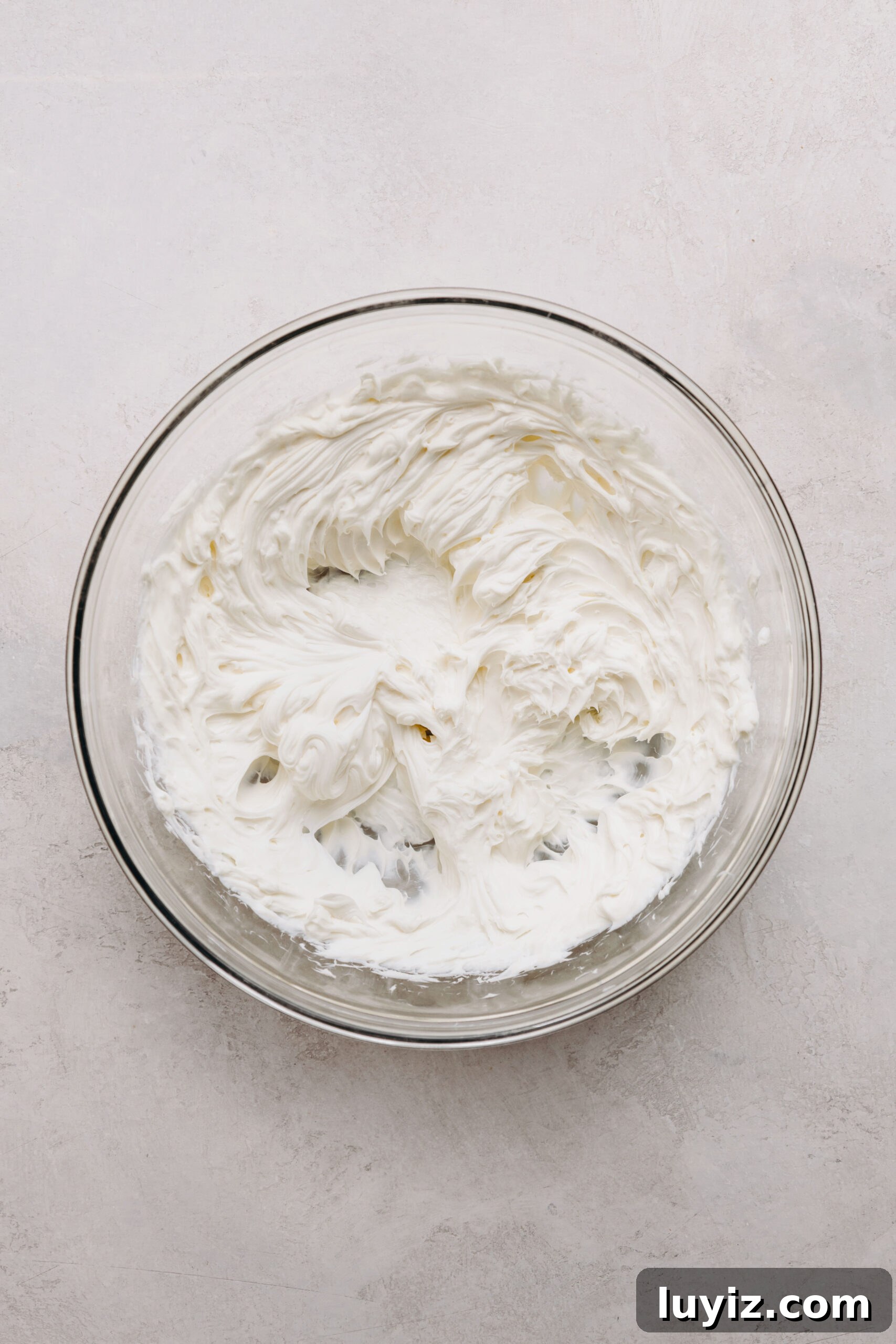 Decadent Black Bottom Cupcakes with Cream Cheese Swirl 6 Softened and beaten cream cheese in a glass mixing bowl on a white marbled background.