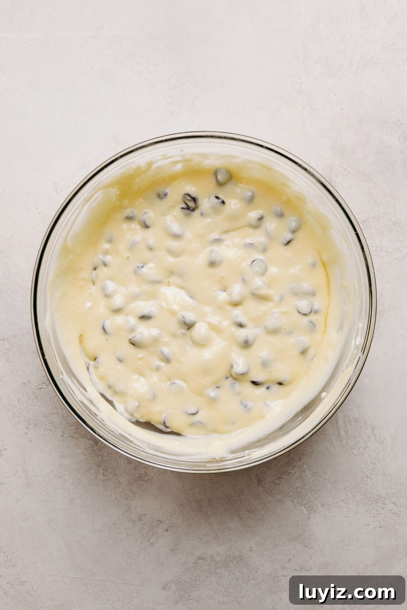 Decadent Black Bottom Cupcakes with Cream Cheese Swirl 7 Chocolate chips folded into cream cheese filling in a glass mixing bowl on a white marbled background.